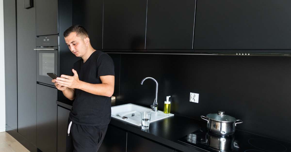 Man checking phone in modern kitchen about cost to replace water softener and home plumbing options.