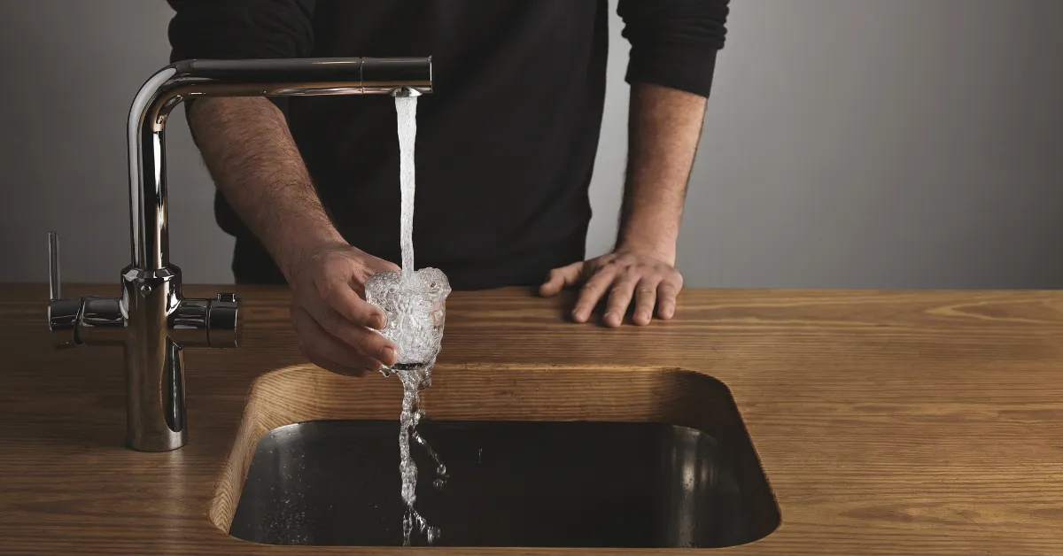 Man filling glass at kitchen sink, water cost for water softener system and home plumbing guide